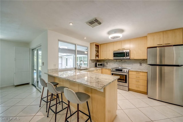 kitchen with sink, stainless steel appliances, light stone counters, kitchen peninsula, and light brown cabinets