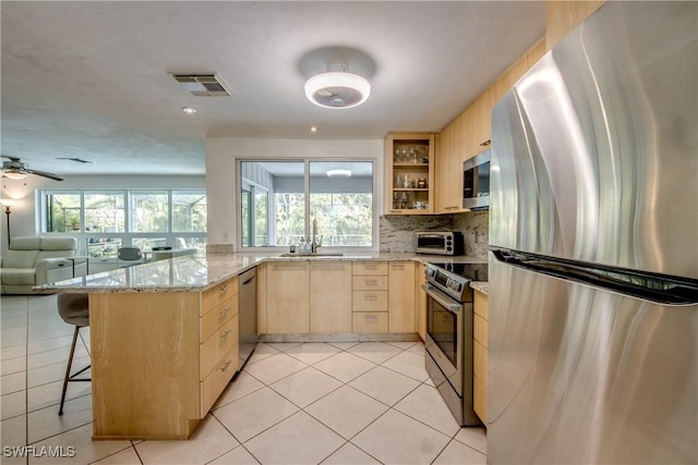 kitchen with a breakfast bar area, light stone counters, light brown cabinets, kitchen peninsula, and stainless steel appliances