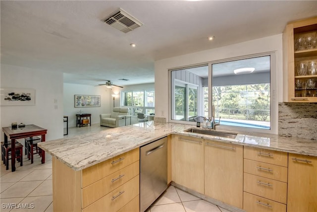 kitchen featuring light brown cabinetry, light tile patterned floors, stainless steel dishwasher, kitchen peninsula, and light stone countertops