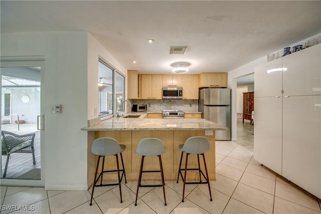 kitchen with appliances with stainless steel finishes, light brown cabinetry, sink, decorative backsplash, and kitchen peninsula