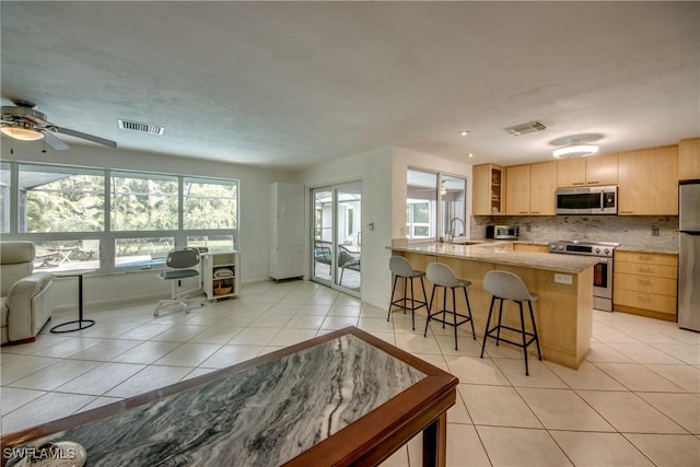 kitchen featuring appliances with stainless steel finishes, a kitchen breakfast bar, light stone counters, kitchen peninsula, and light brown cabinets