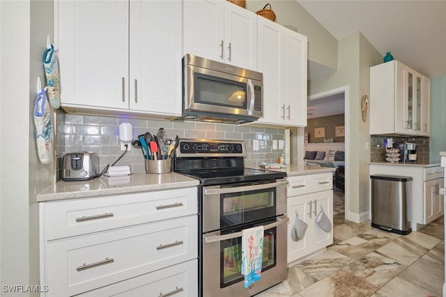 kitchen featuring lofted ceiling, backsplash, white cabinets, light stone countertops, and stainless steel appliances