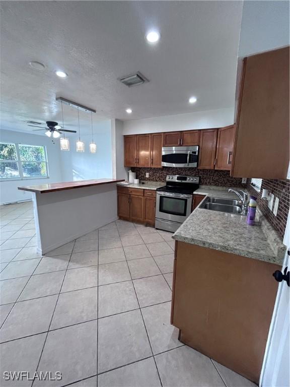 kitchen with kitchen peninsula, stainless steel appliances, ceiling fan, sink, and pendant lighting