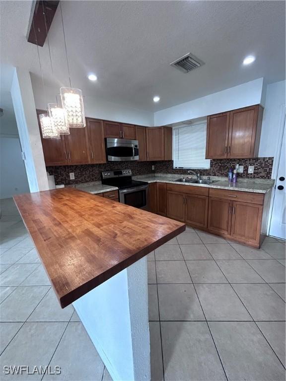 kitchen with wooden counters, kitchen peninsula, stainless steel appliances, decorative light fixtures, and light tile patterned flooring