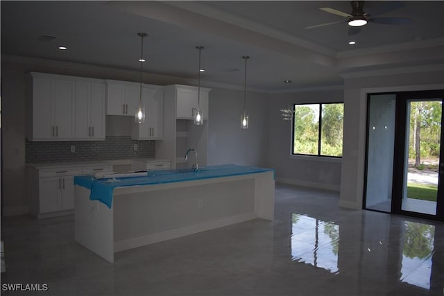 kitchen featuring backsplash, a kitchen island with sink, ceiling fan, pendant lighting, and white cabinets