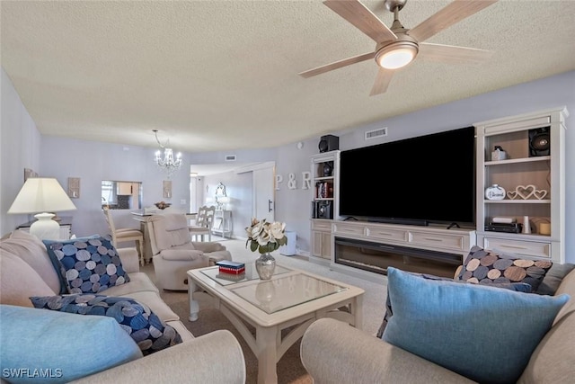 living room featuring a textured ceiling, ceiling fan with notable chandelier, and a fireplace