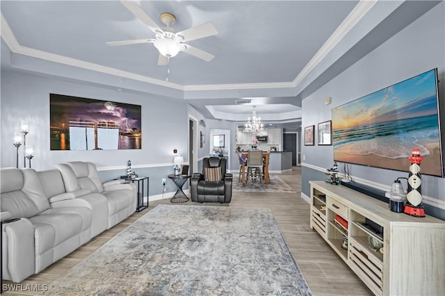 living room featuring ceiling fan with notable chandelier, ornamental molding, and a tray ceiling