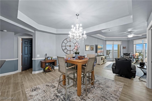 dining space with a raised ceiling and ceiling fan with notable chandelier