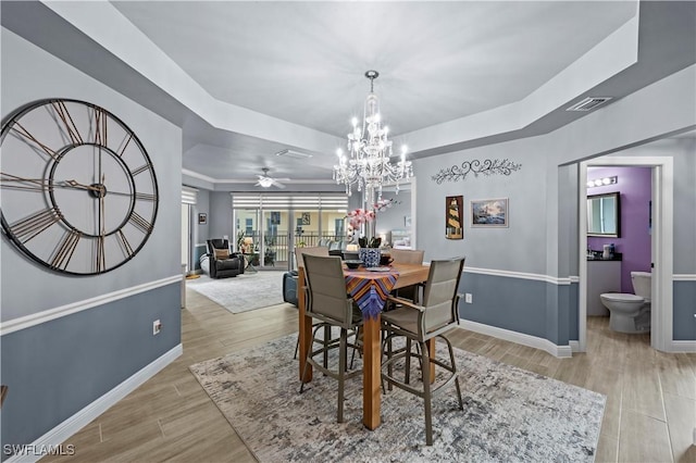 dining area with a raised ceiling and ceiling fan with notable chandelier