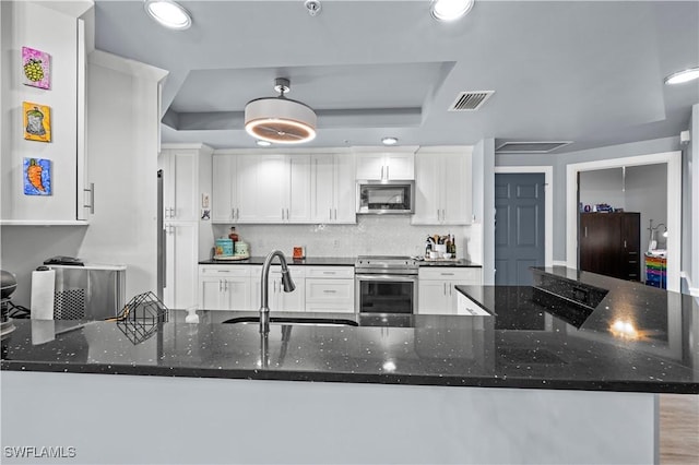 kitchen featuring a tray ceiling, kitchen peninsula, white cabinets, and appliances with stainless steel finishes