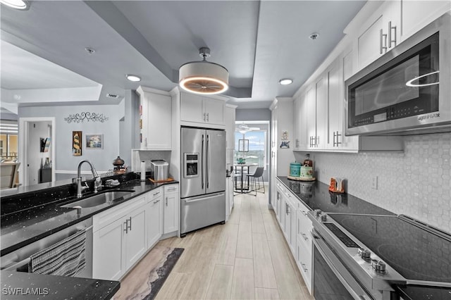 kitchen featuring a tray ceiling, white cabinetry, sink, and appliances with stainless steel finishes