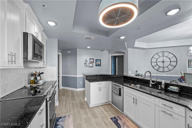 kitchen featuring white cabinets, sink, dark stone countertops, appliances with stainless steel finishes, and a tray ceiling