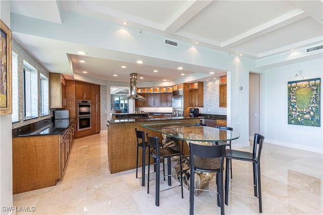 kitchen with a breakfast bar, island range hood, dark stone countertops, a large island with sink, and appliances with stainless steel finishes