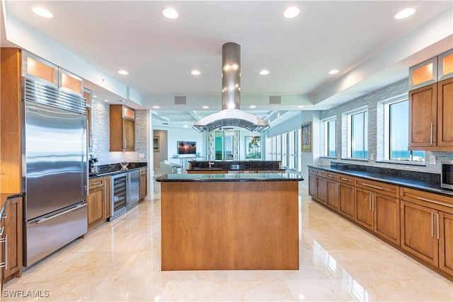 kitchen with built in fridge, dark stone countertops, wine cooler, island exhaust hood, and a large island