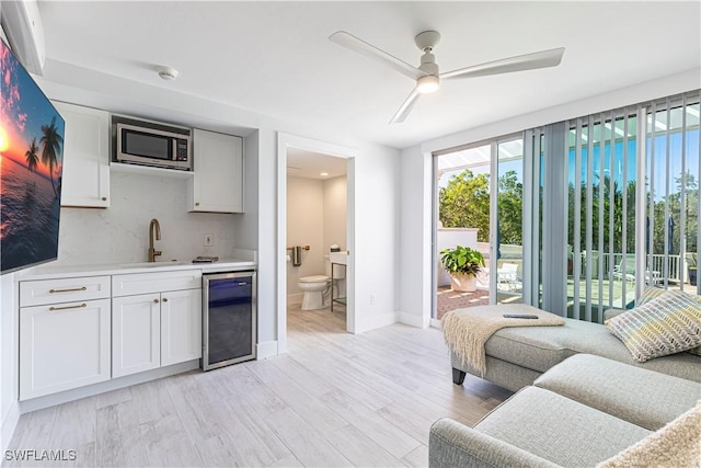 living room featuring indoor wet bar, light hardwood / wood-style floors, beverage cooler, and ceiling fan