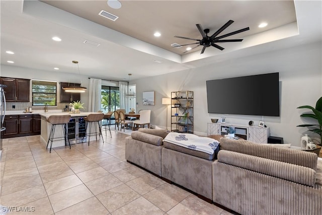 tiled living room with ceiling fan and a raised ceiling