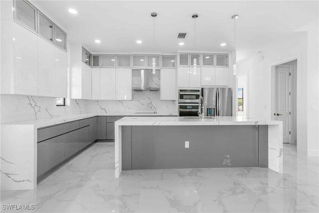 kitchen featuring white cabinets, a spacious island, wall chimney range hood, stainless steel refrigerator with ice dispenser, and decorative light fixtures