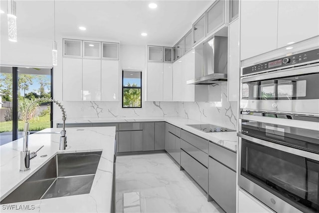 kitchen featuring double wall oven, light stone counters, decorative light fixtures, black electric stovetop, and white cabinets