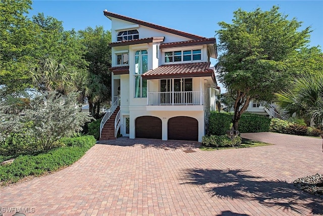 view of front of property with an attached garage, stucco siding, stairs, a tile roof, and decorative driveway