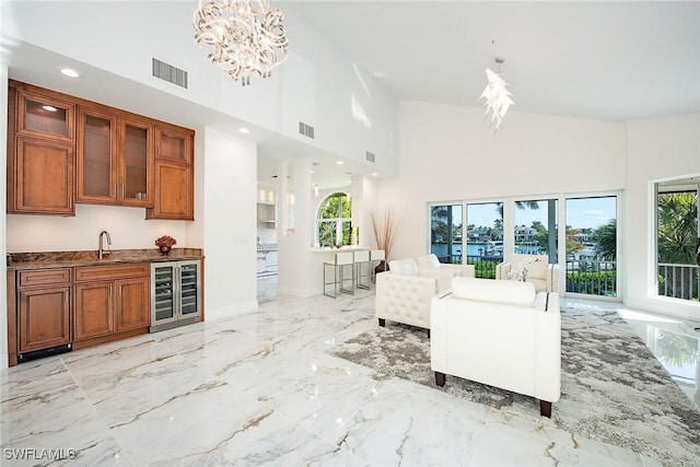 living room featuring wine cooler, sink, a towering ceiling, and a notable chandelier