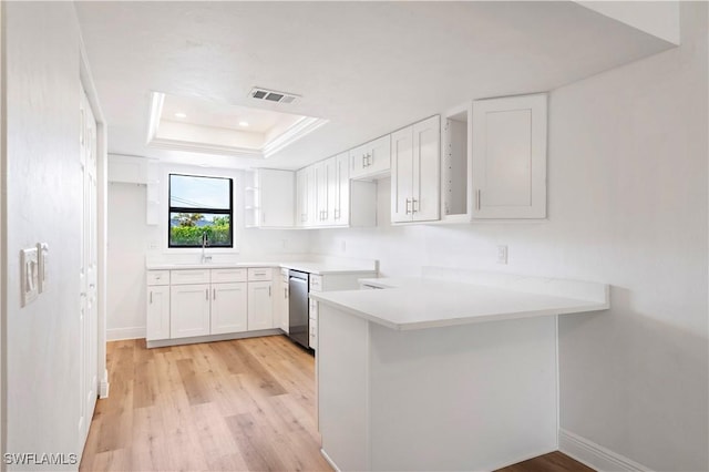 kitchen featuring white cabinetry, light hardwood / wood-style flooring, stainless steel dishwasher, kitchen peninsula, and a tray ceiling