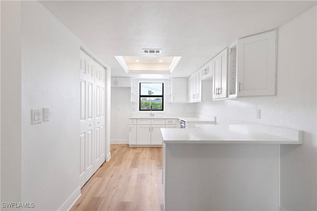 kitchen with sink, a raised ceiling, kitchen peninsula, white cabinets, and light wood-type flooring