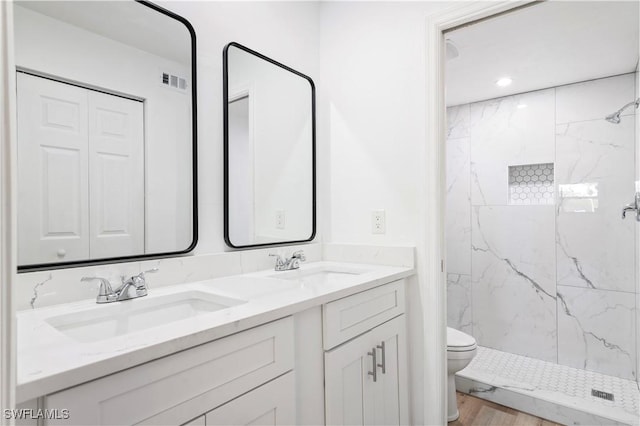 bathroom featuring a tile shower, hardwood / wood-style floors, vanity, and toilet