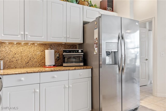 kitchen with stainless steel fridge, backsplash, light stone counters, light tile patterned floors, and white cabinetry