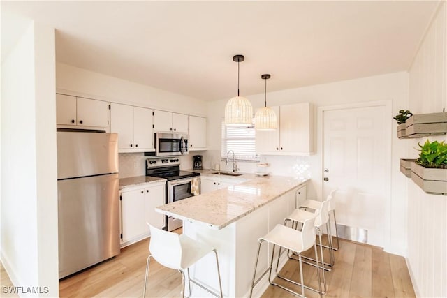 kitchen with sink, hanging light fixtures, stainless steel appliances, a breakfast bar area, and white cabinets