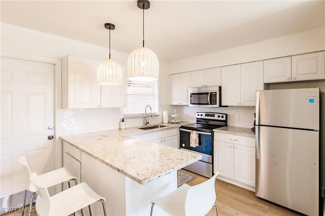 kitchen with appliances with stainless steel finishes, sink, white cabinets, light hardwood / wood-style floors, and a breakfast bar area