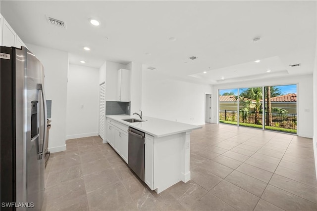 kitchen with kitchen peninsula, appliances with stainless steel finishes, decorative backsplash, sink, and white cabinetry