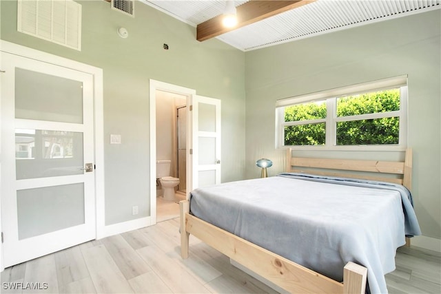 bedroom with beam ceiling, light wood-type flooring, and connected bathroom