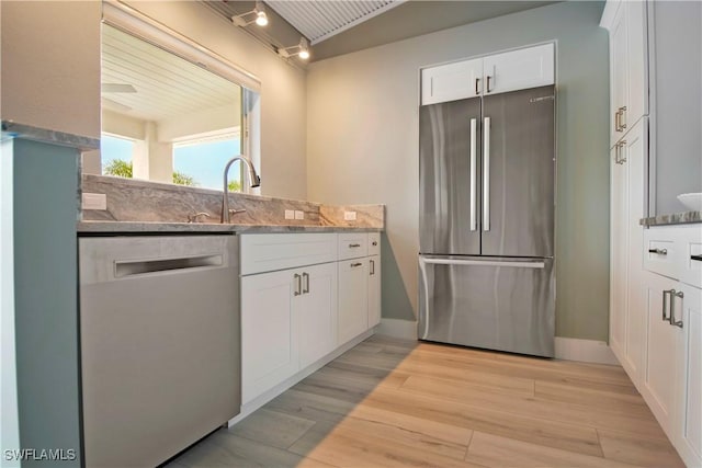 kitchen with light stone countertops, sink, stainless steel appliances, white cabinets, and light wood-type flooring