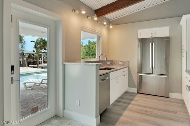 kitchen with light stone countertops, appliances with stainless steel finishes, sink, white cabinets, and vaulted ceiling with beams