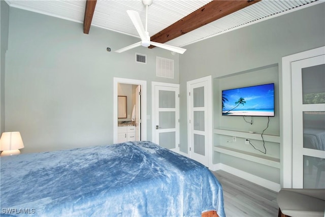 bedroom with ensuite bathroom, beamed ceiling, and light wood-type flooring