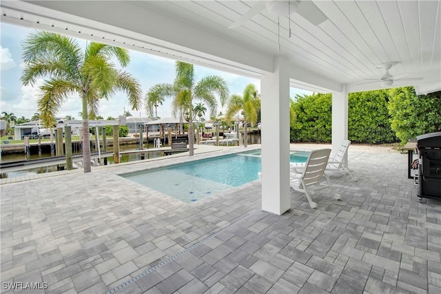 view of swimming pool featuring area for grilling, ceiling fan, a dock, and a water view