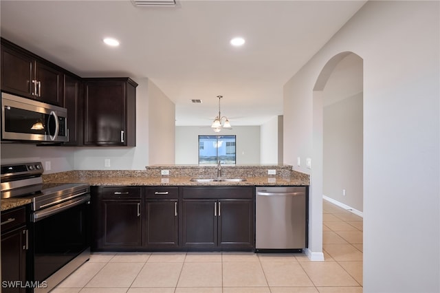 kitchen featuring sink, light tile patterned floors, appliances with stainless steel finishes, dark brown cabinets, and light stone countertops