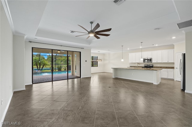 unfurnished living room with a raised ceiling, ceiling fan, crown molding, and sink