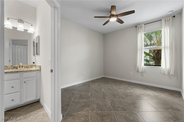 unfurnished room with ceiling fan, dark tile patterned floors, and sink