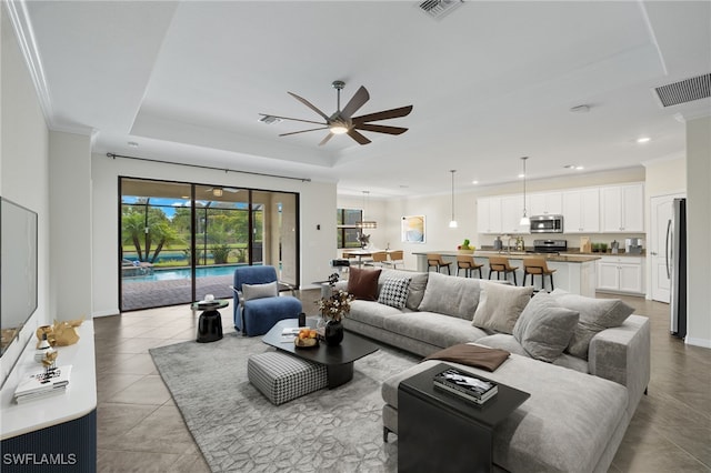 living room featuring a raised ceiling, ceiling fan, light tile patterned floors, and ornamental molding