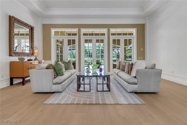 living room featuring french doors, light hardwood / wood-style flooring, a raised ceiling, and ornamental molding