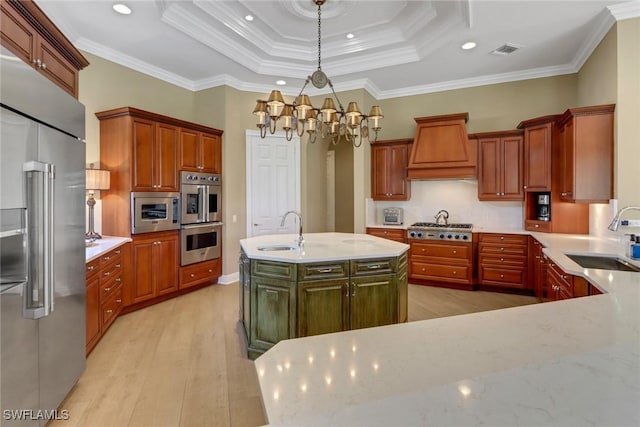 kitchen with pendant lighting, a center island with sink, sink, built in appliances, and ornamental molding