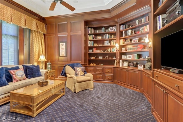 living area featuring crown molding, built in features, ceiling fan, and dark carpet