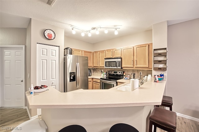 kitchen featuring light hardwood / wood-style floors, a breakfast bar, kitchen peninsula, appliances with stainless steel finishes, and light brown cabinets