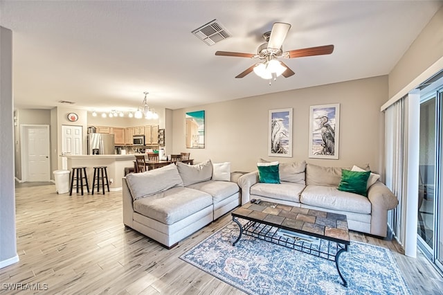 living room with ceiling fan with notable chandelier and light wood-type flooring