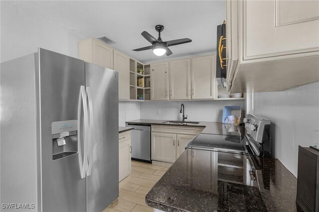 kitchen with stainless steel appliances, ceiling fan, dark stone countertops, and sink