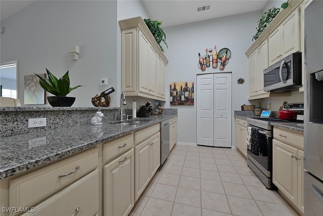 kitchen featuring light tile patterned floors, dark stone counters, appliances with stainless steel finishes, cream cabinetry, and sink