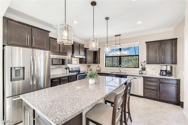 kitchen with light stone countertops, hanging light fixtures, a center island, crown molding, and appliances with stainless steel finishes