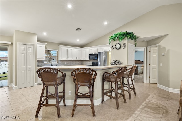 kitchen featuring backsplash, a breakfast bar, black appliances, white cabinets, and lofted ceiling