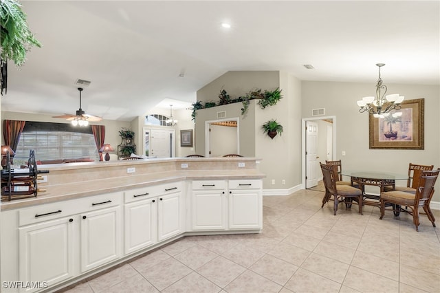 kitchen with hanging light fixtures, white cabinets, vaulted ceiling, light tile patterned floors, and ceiling fan with notable chandelier